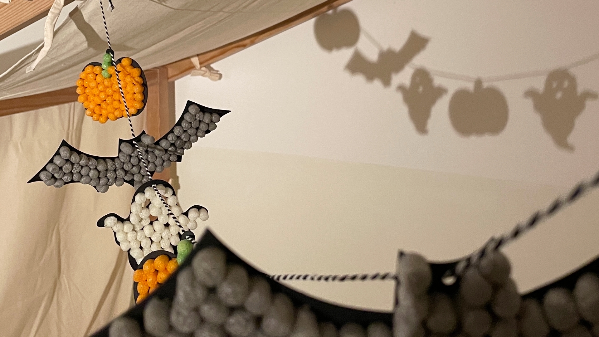 Geister-Kürbis-Fledermaus-Girlande aus Playmais als Deko am Kinderbett.